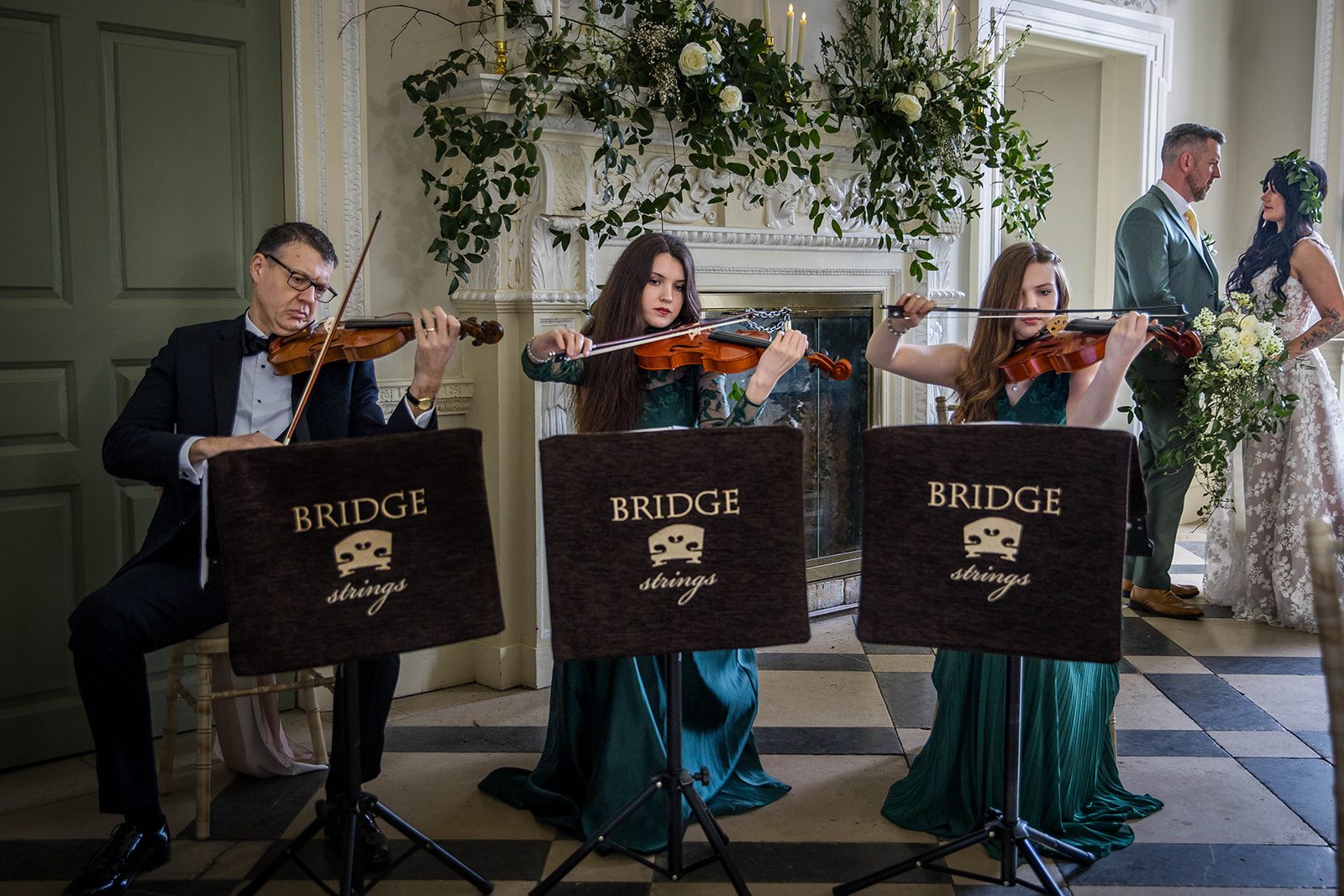 Your wedding ceremony songs may include a string quartet. This image shows 3 violinists playing in front of a couple getting married. 
