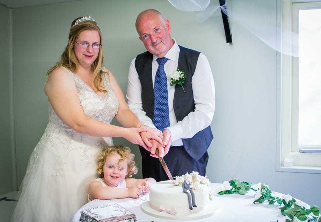 The bride and groom with their daughter cutting the cake at their wedding at The Admiral Hood in Mosterton near Beaminster.